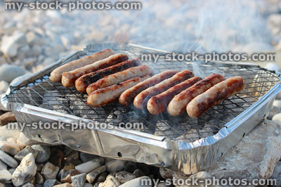 Stock image of disposable barbecue on pebble beach, cooking chipolata sausages