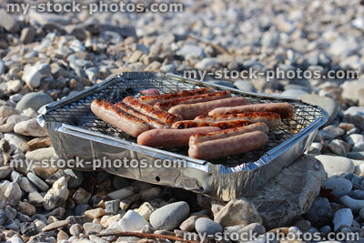 Stock image of sunny pebble beach with hot charcoal barbecue, cooking sausages