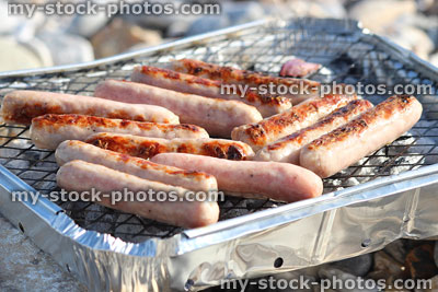 Stock image of raw sausages cooking on beach, disposable charcoal barbecue