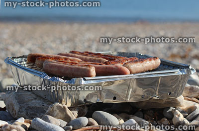 Stock image of pebble beach seaside with disposable barbecue cooking sausages