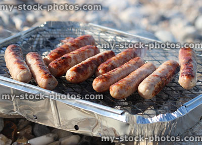 Stock image of disposable party barbecue, foil bbq cooking sausages on beach