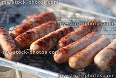 Stock image of sizzling sausages cooking on hot lumpwood disposable barbecue grill