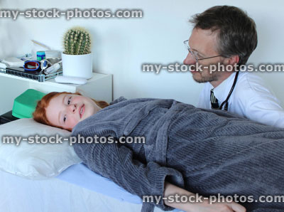Stock image of sick girl lying down on hospital examination bed with doctor