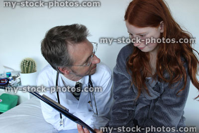 Stock image of hospital doctor showing notes to girl patient on his clipboard