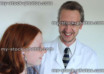 Stock image of young girl in hospital using stethoscope, listening to doctor's heartbeat