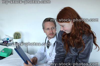 Stock image of hospital doctor showing notes to girl patient on his clipboard