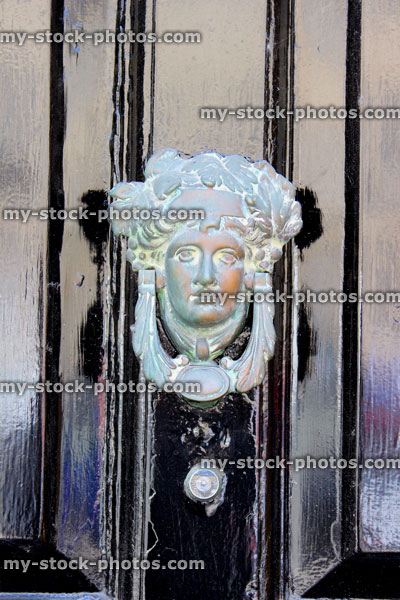 Stock image of ornamental door knocker on black front door, shape of face