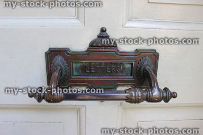 Stock image of ornate copper letterbox on front door with wood panels