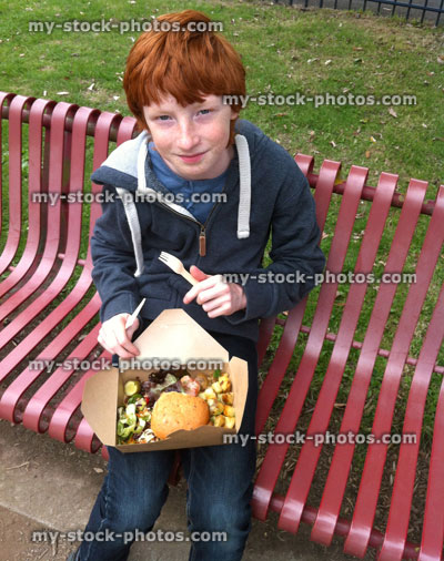 Stock image of boy eating gourmet burger and salad on a park bench