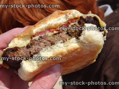 Stock image of boy eating cheeseburger with bacon, holding burger bun