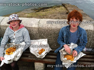 Stock image of children enjoying fish and chips out of paper at harbour