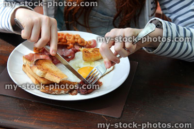 Stock image of girl eating full English fried breakfast, sausage, bacon