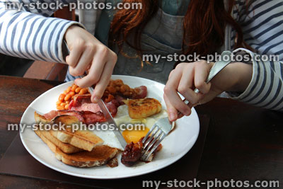 Stock image of girl eating full English fried breakfast, sausage, egg, bacon, baked beans