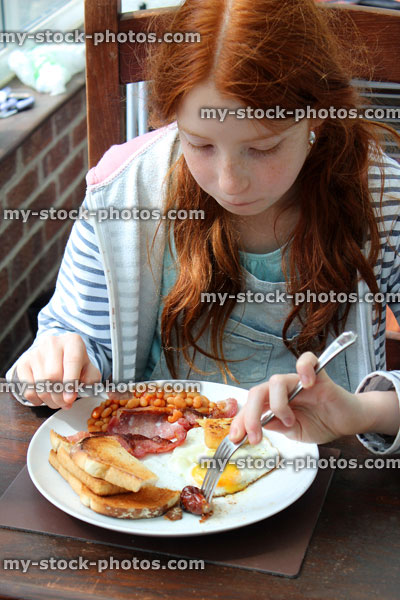 Stock image of girl eating full English fried breakfast, baked beans, sausage