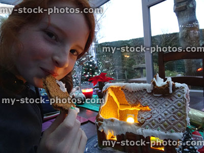 Stock image of girl eating roof of homemade Christmas gingerbread house
