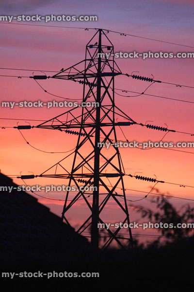 Stock image of tall high voltage electricity pylon against orange sunset sky