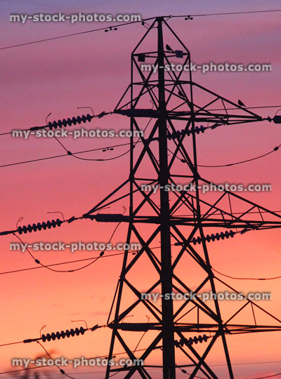 Stock image of tall high voltage electricity pylon against orange sunset sky