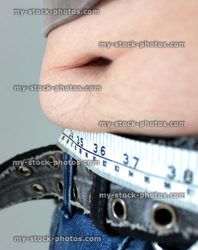 Stock image of overweight man with a fat tummy spilling over jeans, measuring tape