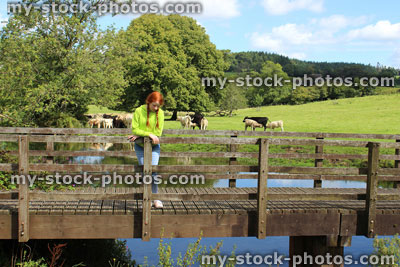 Stock image of girl standing on wooden bridge, countryside, looking down at river