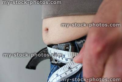 Stock image of overweight man with a fat tummy spilling over jeans, measuring