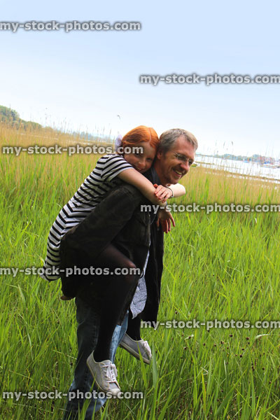 Stock image of father playing with daughter, having fun piggy back, carrying her