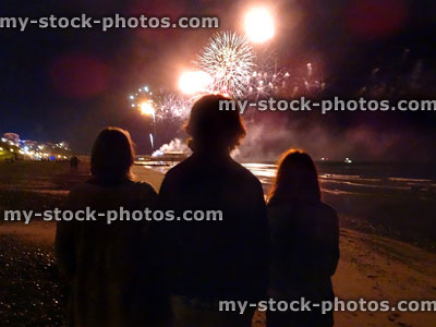 Stock image of family silhouettes watching seaside fireworks display on beach