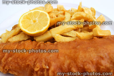 Stock image of battered fish and chips on a white plate with lemon