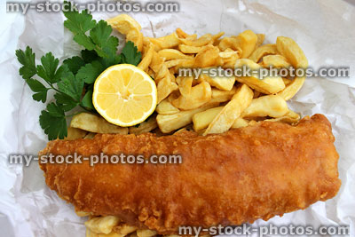 Stock image of fish and chips in white paper with lemon and parsley