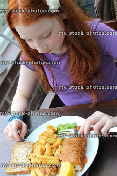 Stock image of girl eating a plate of fish and chips, mushy peas
