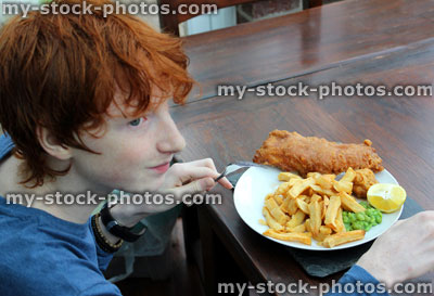 Stock image of boy eating a plate of fish and chips, mushy peas