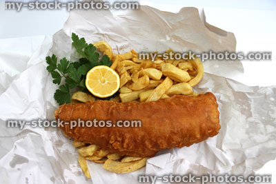 Stock image of battered fish and chips in white paper with parsley