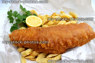 Stock image of fish and chips in white paper with lemon and parsley