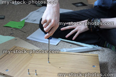 Stock image of teenage boy assembling flatpack furniture cabinet, DIY with screwdriver, screws