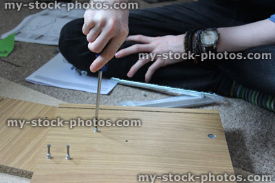 Stock image of teenage boy assembling flatpack furniture cabinet, DIY with screwdriver, screws
