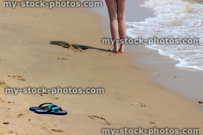 Stock image of girl's legs by sea, barefoot on beach, flip flops, thongs, sand