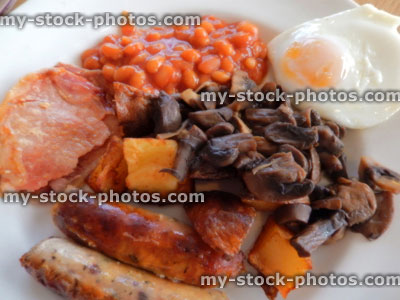 Stock image of fried breakfast with sausages, bacon, fried potatoes, fried egg, baked beans, mushrooms