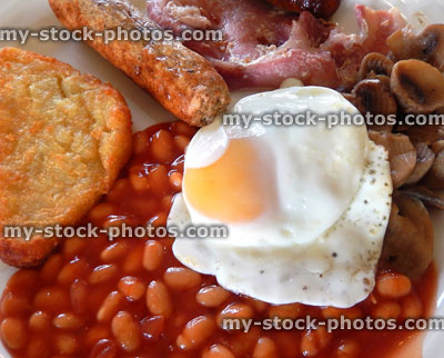 Stock image of fried breakfast / fry up, sausages, bacon, hash brown, mushrooms, fried egg, baked beans
