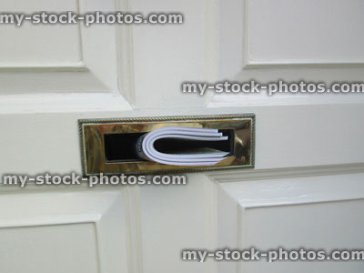 Stock image of white front door, wooden panels, magazines pushed through brass letterbox