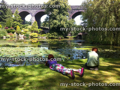 Stock image of young children relaxing by pond in landscaped garden