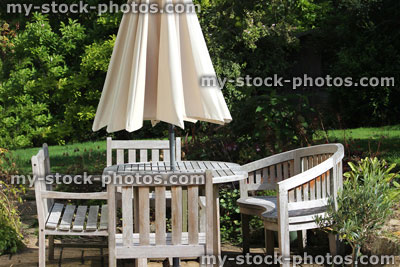 Stock image of wooden garden furniture, teak table, bench, chairs, parasol