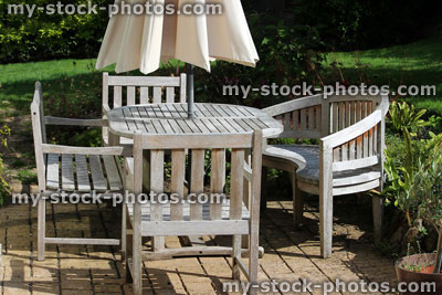 Stock image of wooden garden furniture, teak table, bench, chairs, parasol