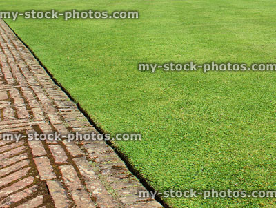 Stock image of mown garden lawn grass edged with red brick, block paving path