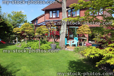 Stock image of green lawn in back garden, red brick house, patio furniture