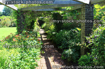 Stock image of red brick path through herbaceous flower border, cottage garden, wooden pergola