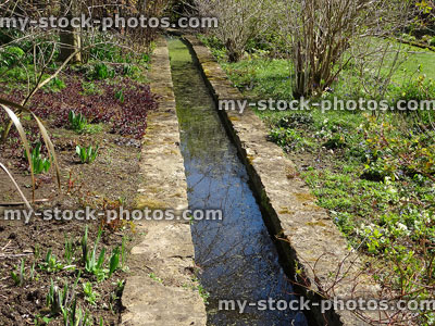Stock image of small stream running through garden, lined with flagstones