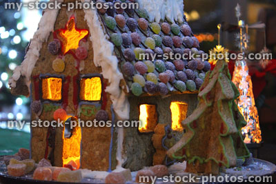Stock image of night time gingerbread house, lit with tealight candles, Christmas trees