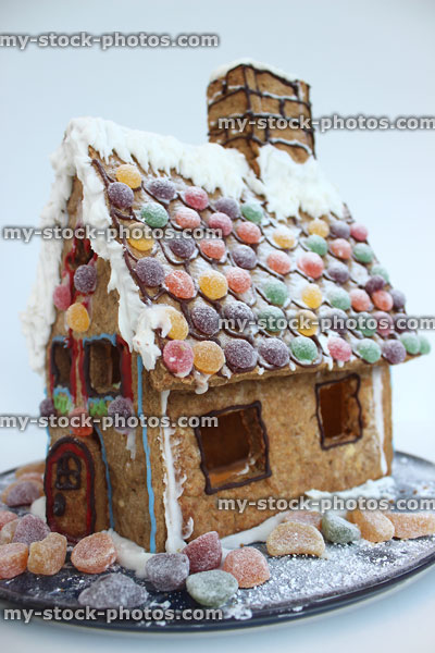 Stock image of decorated gingerbread house on plate with sweets, icing sugar