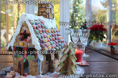 Stock image of gingerbread house on wooden table with sweets, poinsettias