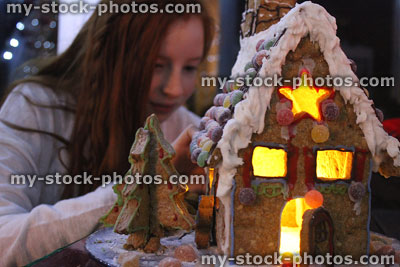 Stock image of girl sticking sweets on illuminated biscuit gingerbread house