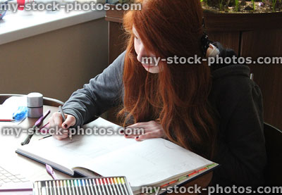Stock image of girl drawing with coloured pencils at table, art homework
